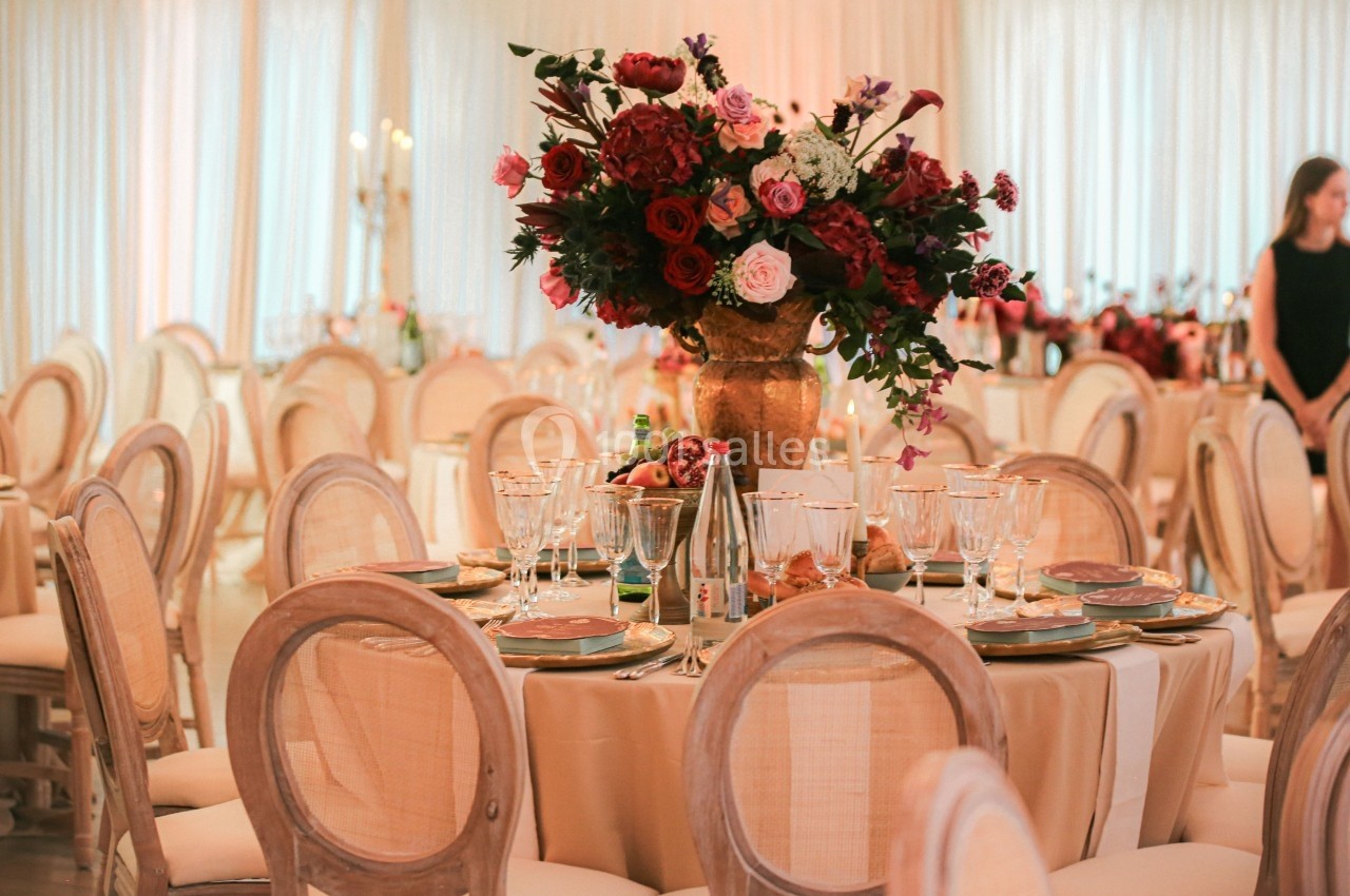 Table élégamment dressée avec des chaises en bois clair, un grand bouquet de fleurs rouges et roses au centre.