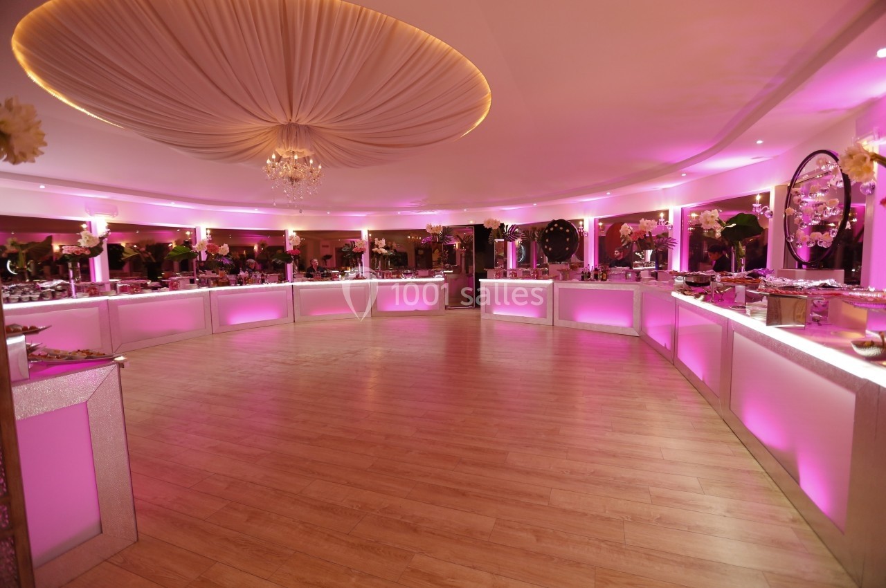 Location salle Le Coudray-Montceaux (Essonne) - Le Manoir des Cygnes #19 Salle de réception circulaire avec éclairage rose, tables de buffet alignées et plafond orné d'un drapé central.