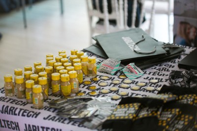 Salle lumineuse avec des stands promotionnels, des affiches et des tables recouvertes de nappes bleues, entourées de chaises…