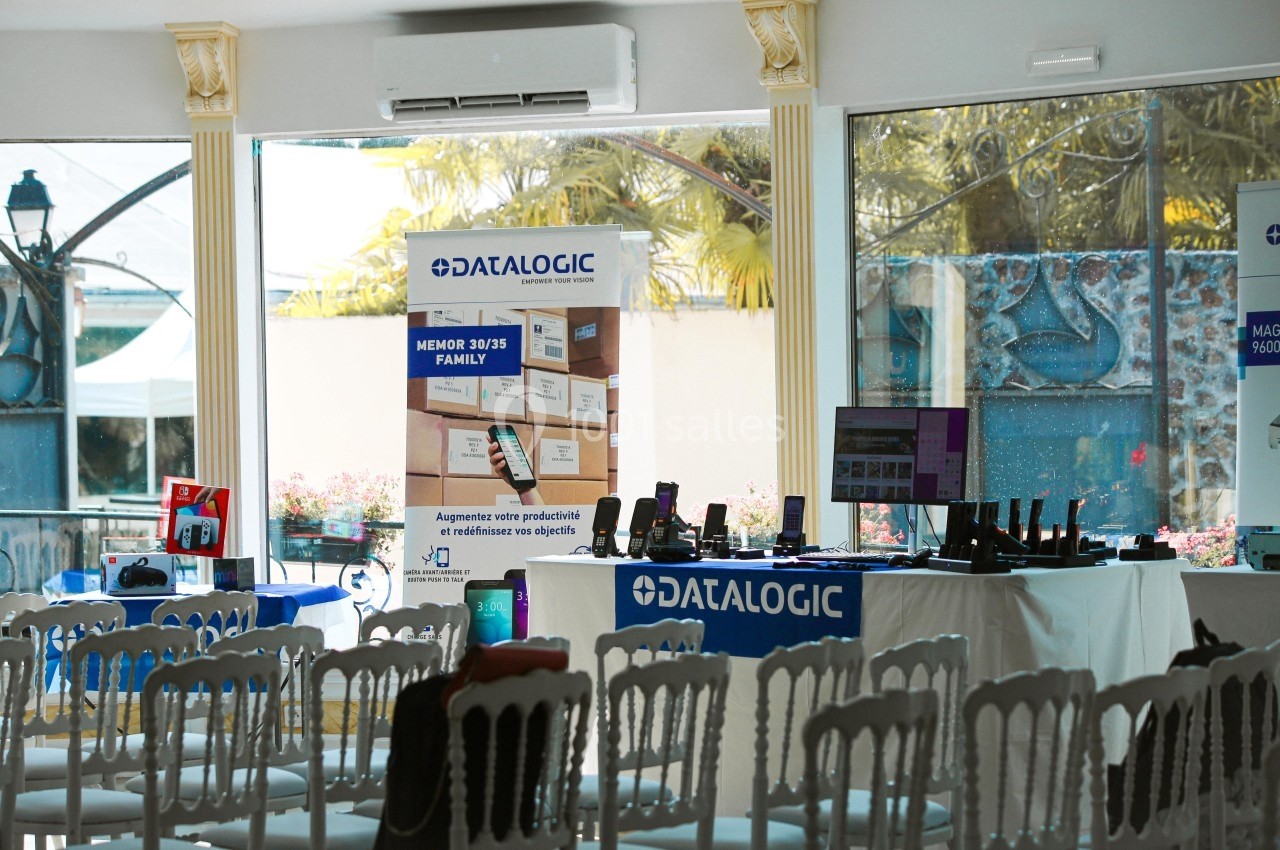 Salle équipée de chaises blanches, avec des stands présentant des produits technologiques et des affiches promotionnelles.