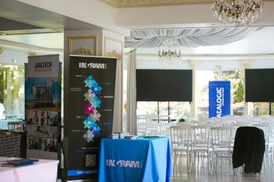 Salle lumineuse avec des stands promotionnels, des affiches et des tables recouvertes de nappes bleues, entourées de chaises…
