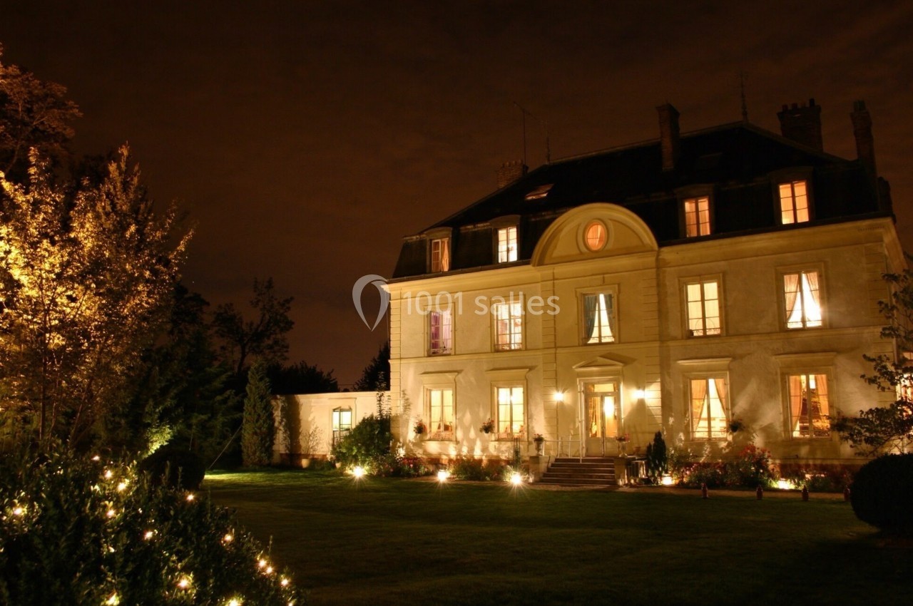 Location salle Le Coudray-Montceaux (Essonne) - Le Manoir des Cygnes #4 Manoir éclairé la nuit, entouré d'un jardin avec des lumières décoratives et des arbres.