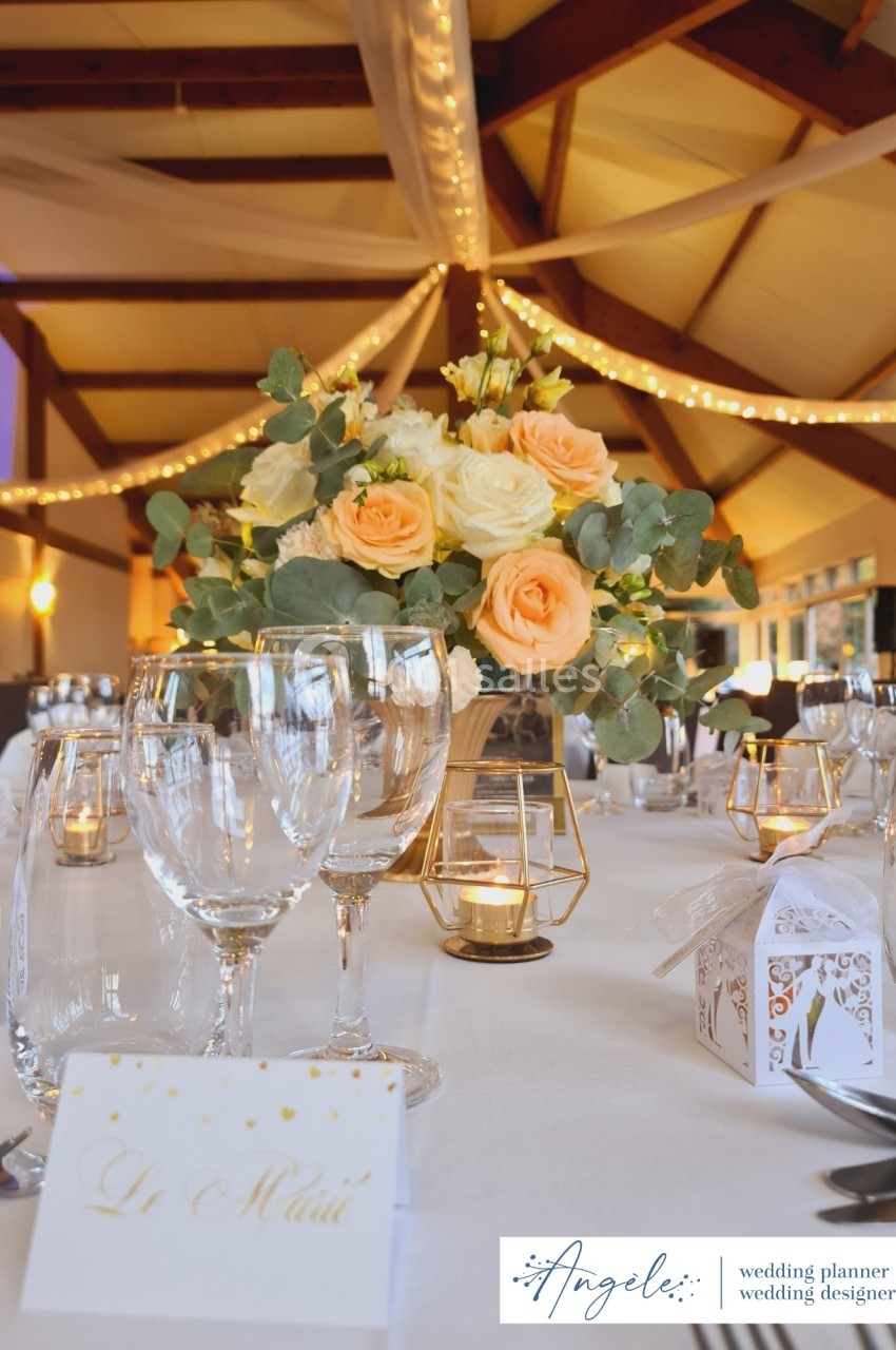Table de mariage décorée avec des roses, des bougies dorées et des cadeaux d'invités, sous un plafond illuminé.