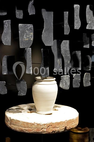 Vase en céramique blanche posé sur un tour de potier, entouré de fragments de pierre suspendus.