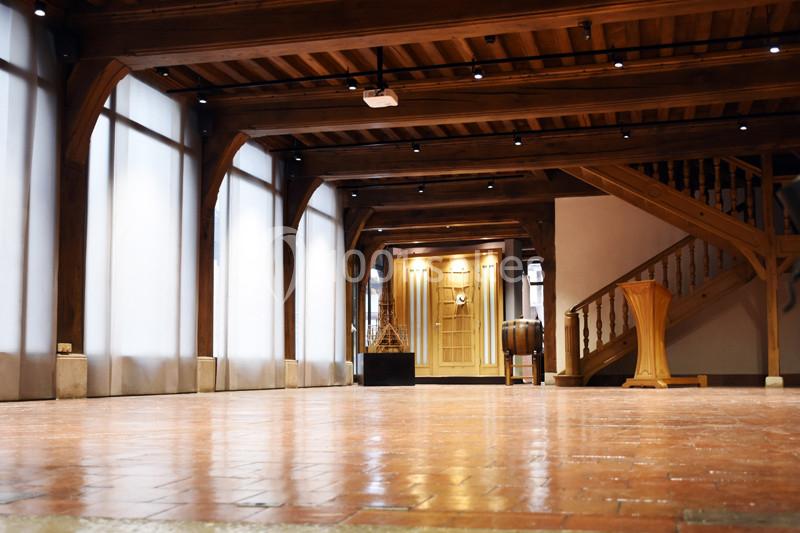 Intérieur d'une salle avec poutres en bois, sol en carrelage, escalier en bois et éclairage tamisé.
