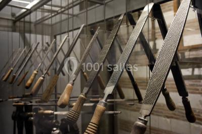Rangée de limes métalliques suspendues avec des manches en bois dans un atelier ou une exposition artisanale.