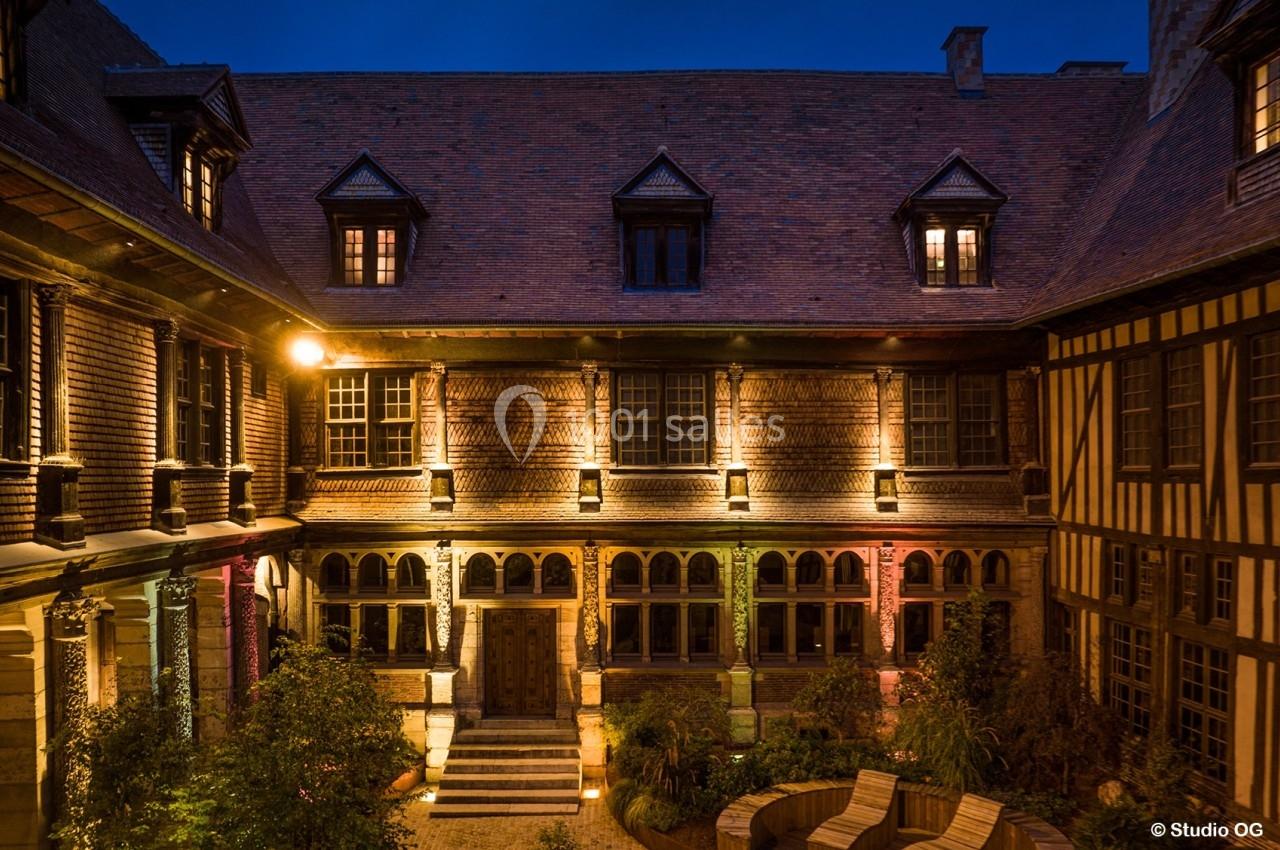 Cour intérieure d'un bâtiment historique à colombages, éclairée par des lumières chaleureuses en soirée.