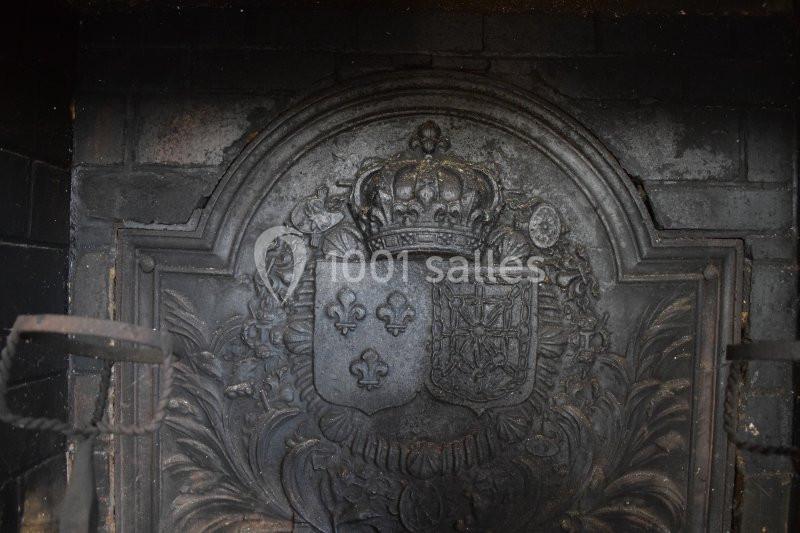 Plaque en fonte ornée d'armoiries et d'une couronne, intégrée dans un foyer de cheminée noirci.