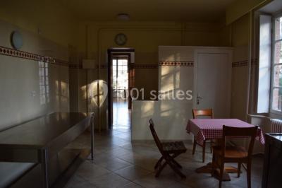 Cuisine lumineuse avec table en bois et nappe à carreaux rouges, chaises, plan de travail en métal et fenêtre ouverte.