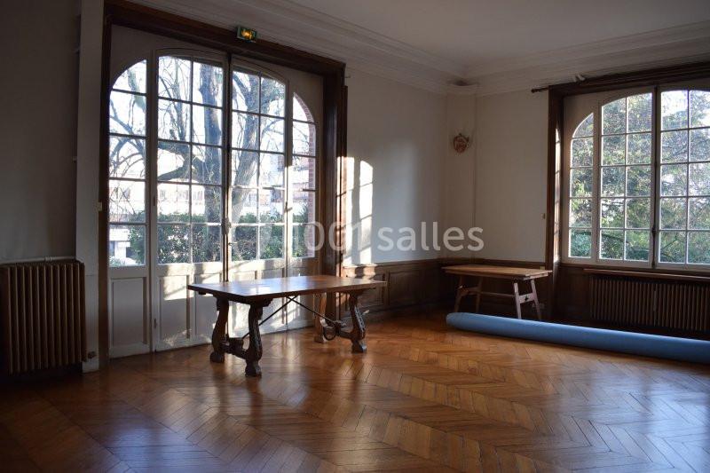 Salle lumineuse avec parquet en bois, grandes fenêtres donnant sur un jardin et mobilier en bois minimaliste.