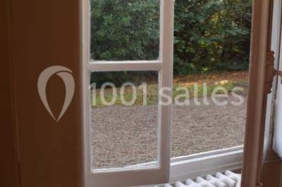 Cuisine lumineuse avec table en bois et nappe à carreaux rouges, chaises, plan de travail en métal et fenêtre ouverte.