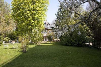 Cuisine lumineuse avec table en bois et nappe à carreaux rouges, chaises, plan de travail en métal et fenêtre ouverte.