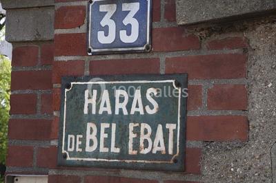 Cuisine lumineuse avec table en bois et nappe à carreaux rouges, chaises, plan de travail en métal et fenêtre ouverte.