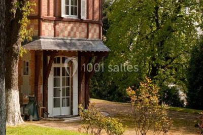 Cuisine lumineuse avec table en bois et nappe à carreaux rouges, chaises, plan de travail en métal et fenêtre ouverte.