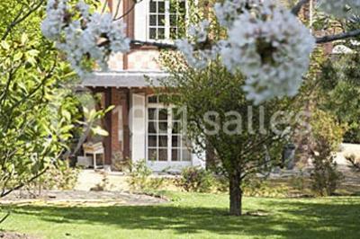 Cuisine lumineuse avec table en bois et nappe à carreaux rouges, chaises, plan de travail en métal et fenêtre ouverte.
