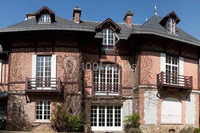 Cuisine lumineuse avec table en bois et nappe à carreaux rouges, chaises, plan de travail en métal et fenêtre ouverte.