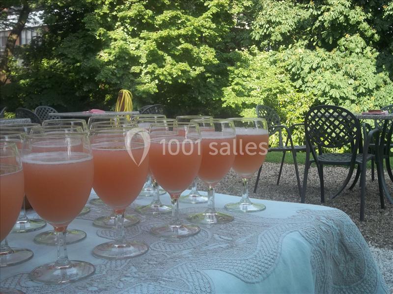 Verres de cocktail rose alignés sur une nappe blanche, avec des tables et un jardin verdoyant en arrière-plan.