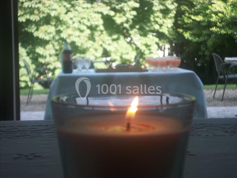 Bougie allumée au premier plan avec une table dressée en extérieur et un jardin verdoyant en arrière-plan.