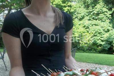Cuisine lumineuse avec table en bois et nappe à carreaux rouges, chaises, plan de travail en métal et fenêtre ouverte.