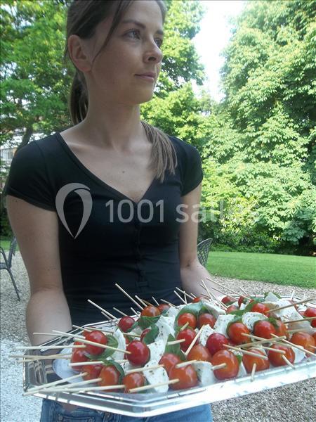 Une femme tenant un plateau de brochettes de tomates, mozzarella et basilic dans un jardin verdoyant.