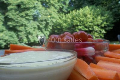 Cuisine lumineuse avec table en bois et nappe à carreaux rouges, chaises, plan de travail en métal et fenêtre ouverte.
