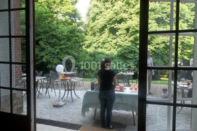 Cuisine lumineuse avec table en bois et nappe à carreaux rouges, chaises, plan de travail en métal et fenêtre ouverte.