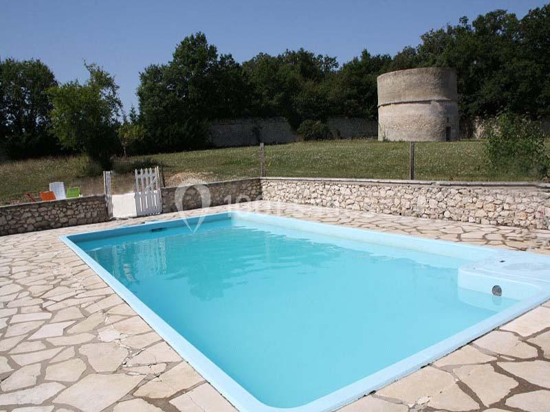 Piscine extérieure rectangulaire entourée d'une terrasse en pierre, avec un jardin et une tour en arrière-plan.