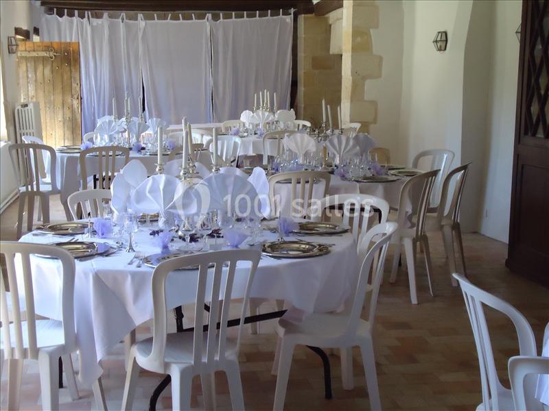 Salle de réception avec tables rondes dressées, nappes blanches, serviettes pliées et chandeliers.