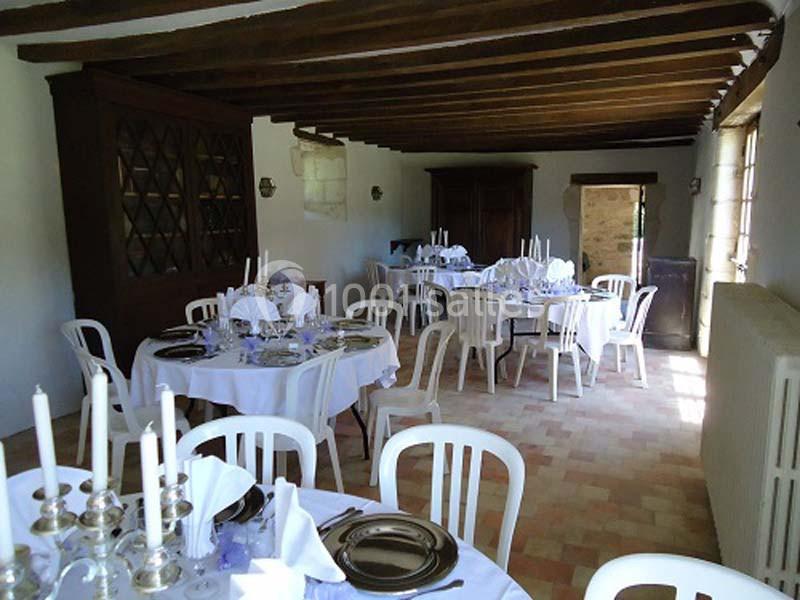 Salle à manger avec tables rondes dressées, chaises blanches, poutres apparentes et lumière naturelle.
