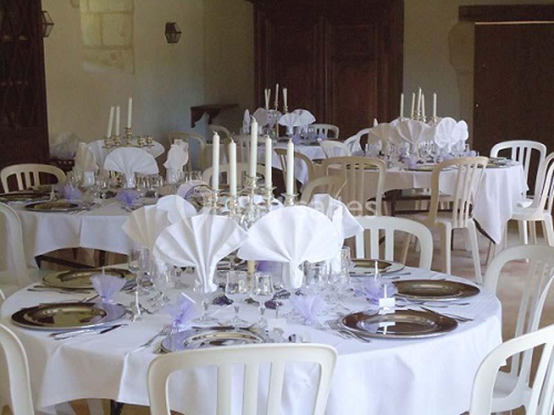 Tables rondes élégamment dressées avec nappes blanches, serviettes pliées et chandeliers dans une salle de réception.