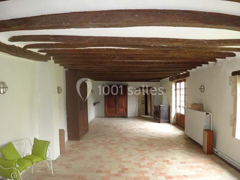 Salle lumineuse avec poutres apparentes, murs blancs, sol en carreaux de terre cuite et mobilier minimaliste.