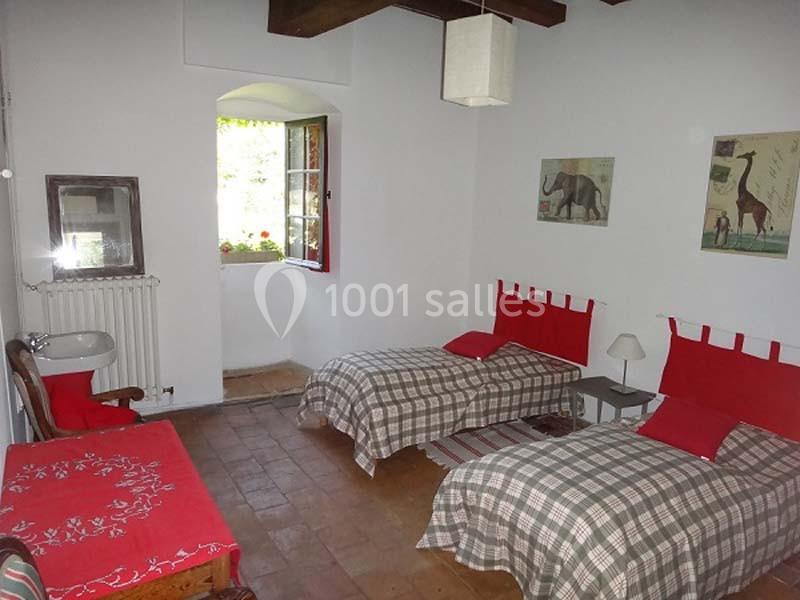 Chambre lumineuse avec deux lits simples, murs blancs, poutres apparentes, fenêtre ouverte et décoration sobre.