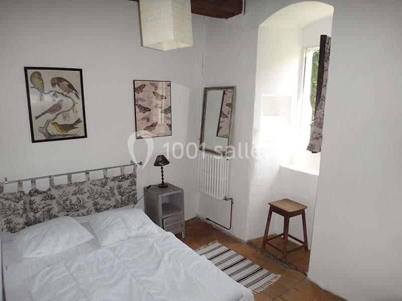 Chambre lumineuse avec lit double, murs blancs décorés de cadres d'oiseaux, fenêtre avec rideaux et mobilier simple.