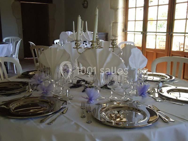 Table élégamment dressée avec nappes blanches, serviettes pliées, chandeliers et vaisselle en métal brillant.