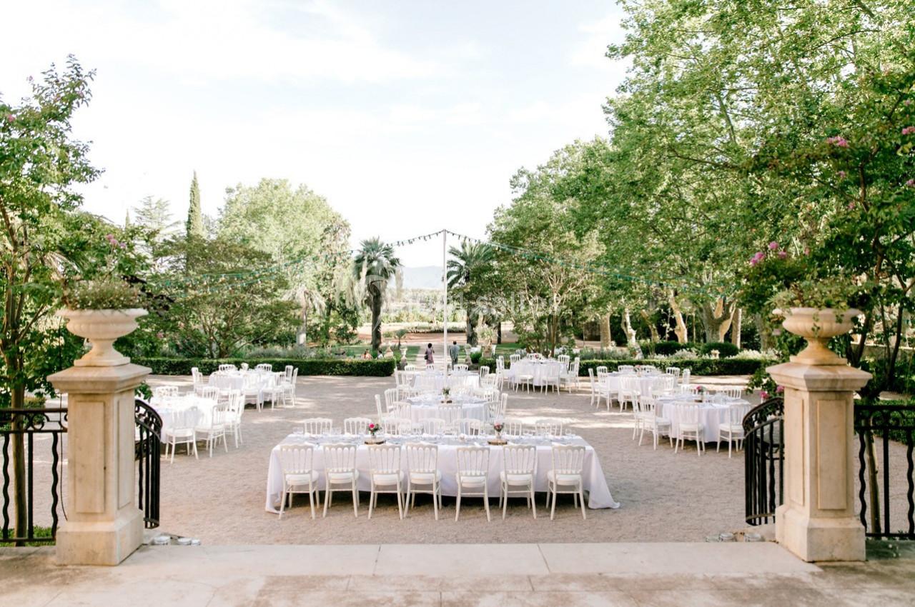 Tables dressées pour un événement en plein air dans un jardin avec des arbres et des guirlandes lumineuses.