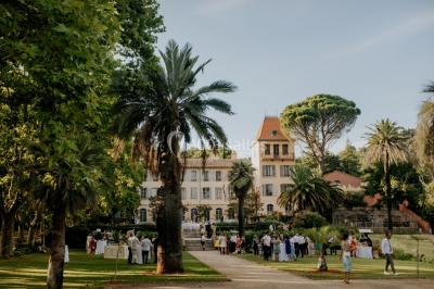 Allée bordée de palmiers éclairés, menant à une fontaine illuminée dans un jardin au crépuscule.