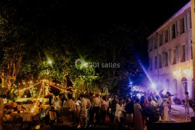 Allée bordée de palmiers éclairés, menant à une fontaine illuminée dans un jardin au crépuscule.