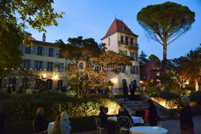Allée bordée de palmiers éclairés, menant à une fontaine illuminée dans un jardin au crépuscule.