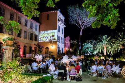 Allée bordée de palmiers éclairés, menant à une fontaine illuminée dans un jardin au crépuscule.