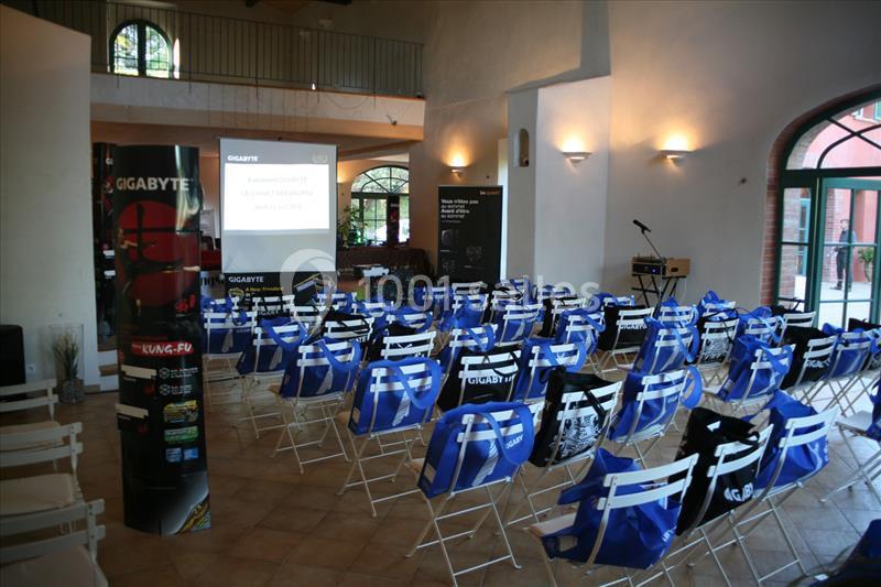 Salle de conférence avec des chaises pliantes alignées, un écran de projection et des affiches promotionnelles.