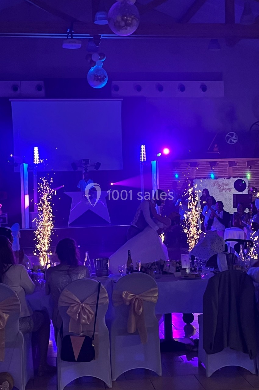 Un couple danse au centre d'une salle de réception éclairée par des lumières colorées et des étincelles.