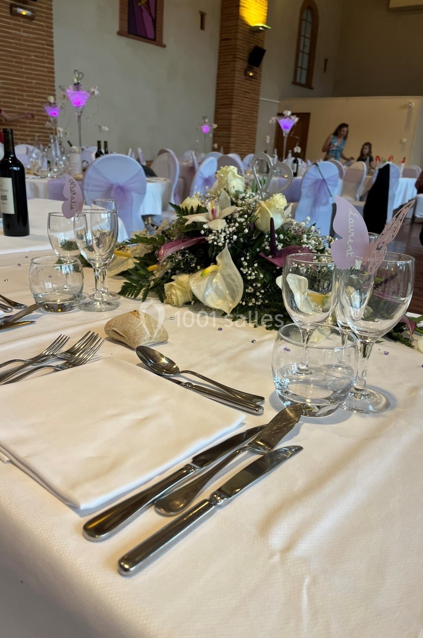 Table élégamment dressée avec des couverts, serviettes blanches, centre de table floral et décorations violettes.