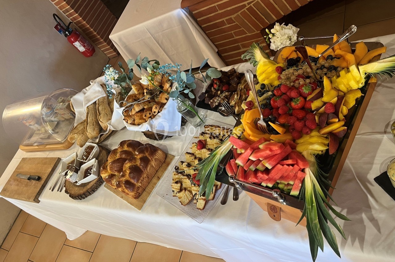 Buffet avec pains, viennoiseries, fruits frais découpés et décorations florales sur une table blanche.