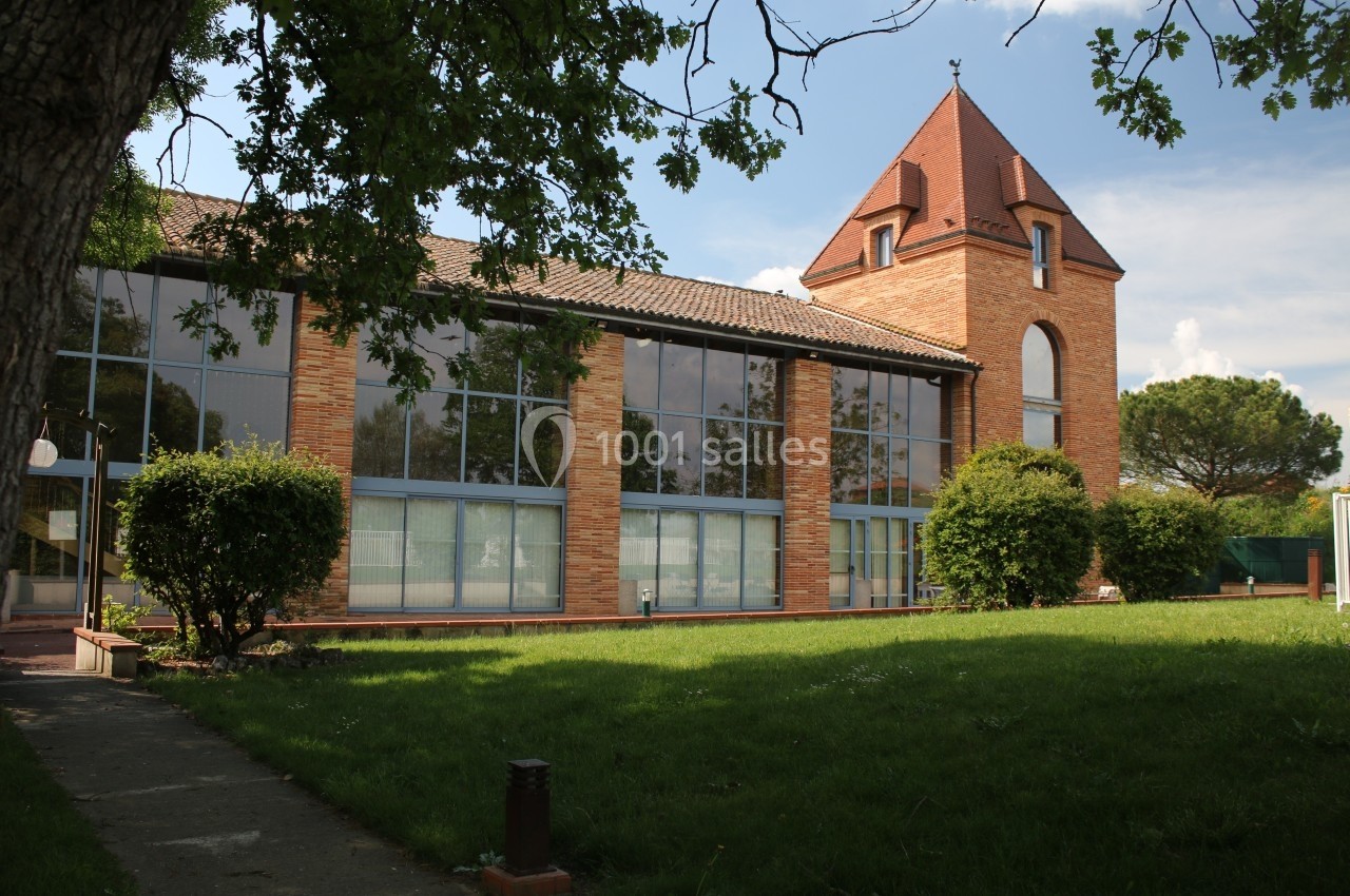 Bâtiment en briques rouges avec de grandes fenêtres, entouré de pelouse et d'arbres sous un ciel partiellement nuageux.