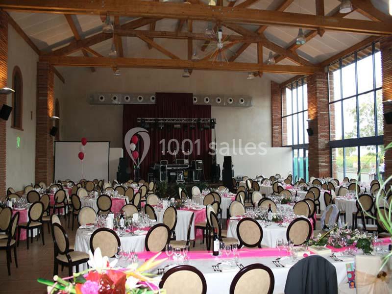 Salle de réception décorée avec des tables dressées, nappes blanches et chemins de table roses, prête pour un événement.