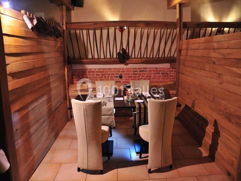 Salle de restaurant avec une table dressée pour quatre personnes, entourée de cloisons en bois et décor rustique.