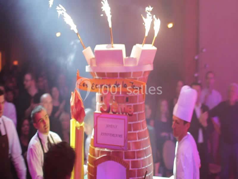Un gâteau en forme de château avec des étincelles, entouré de pâtissiers dans une salle festive.