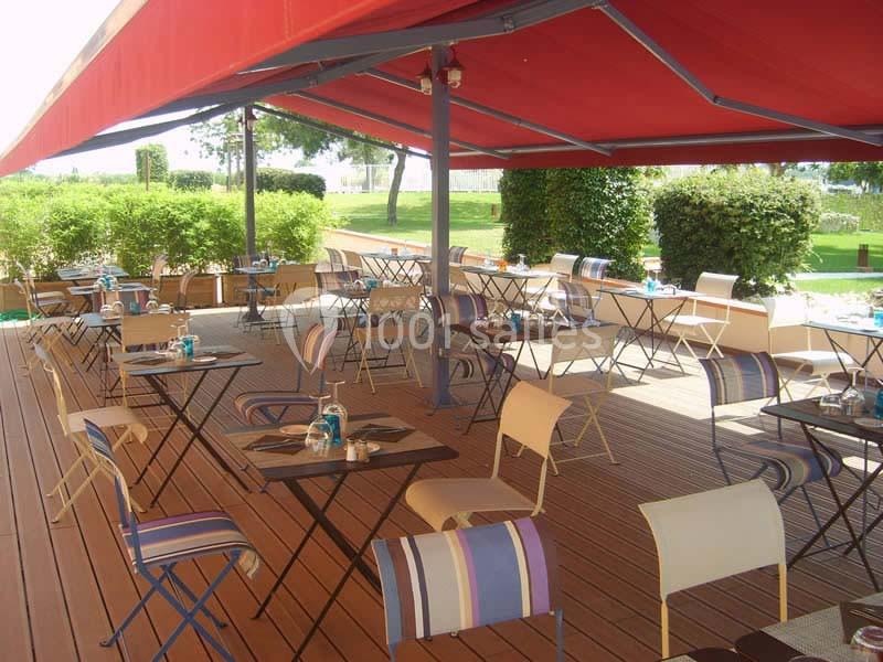 Terrasse extérieure avec tables et chaises colorées sous un auvent rouge, entourée de verdure.