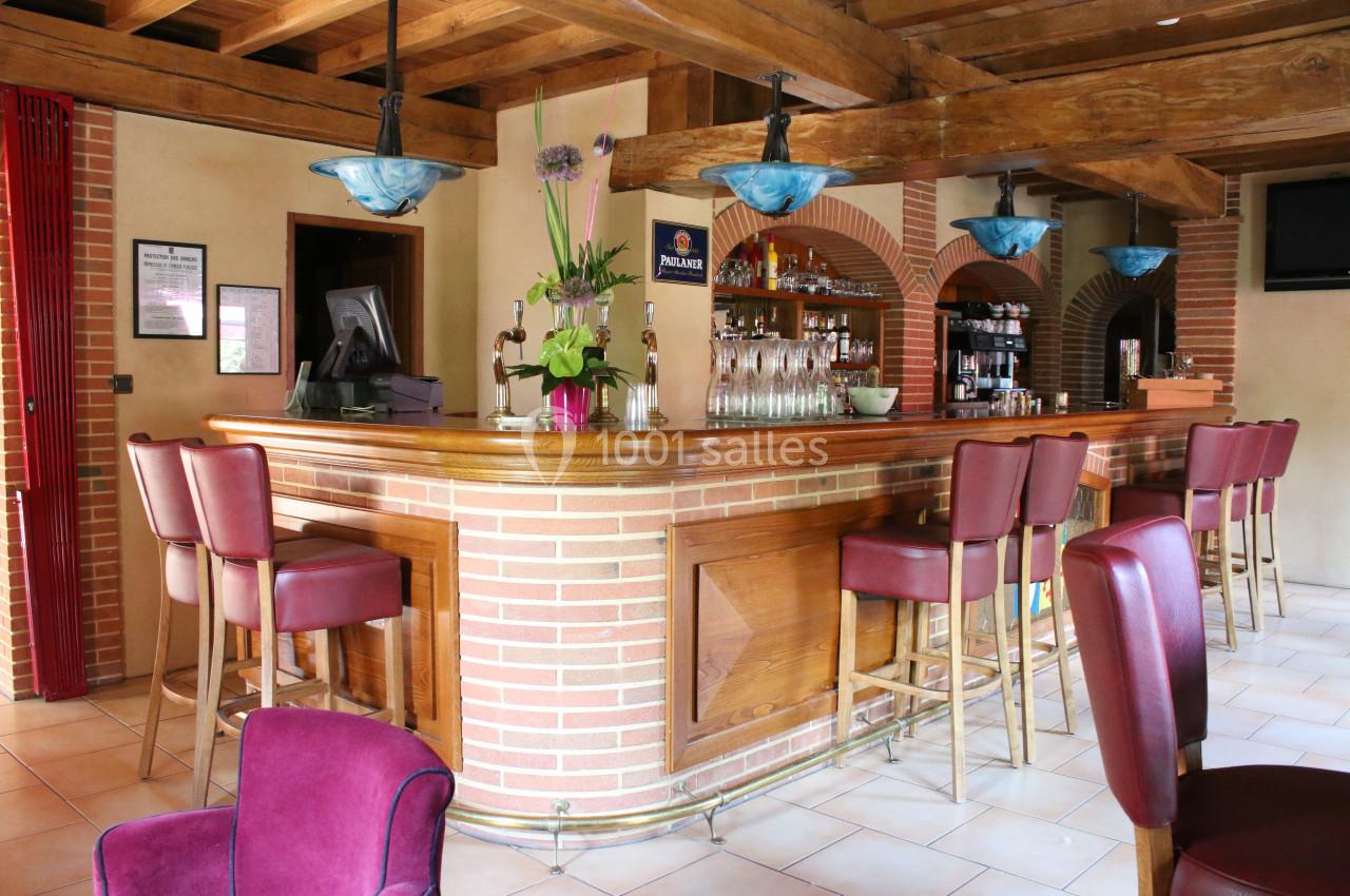 Bar en bois avec comptoir en briques, tabourets rouges, décorations florales et luminaires suspendus.