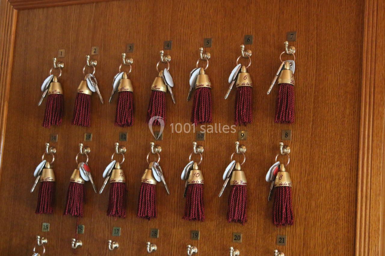 Clés d'hôtel avec porte-clés à pompons rouges accrochées sur un tableau en bois numéroté.